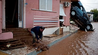 Nov. 15, 2017 photo, a man clears mad from his home in front of flipped over cars in the town of Mandra 