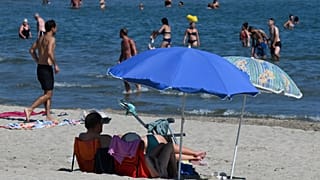 A man and a woman sit on the sand under a parasol on the beach in Palavas-les-Flots, southern France
