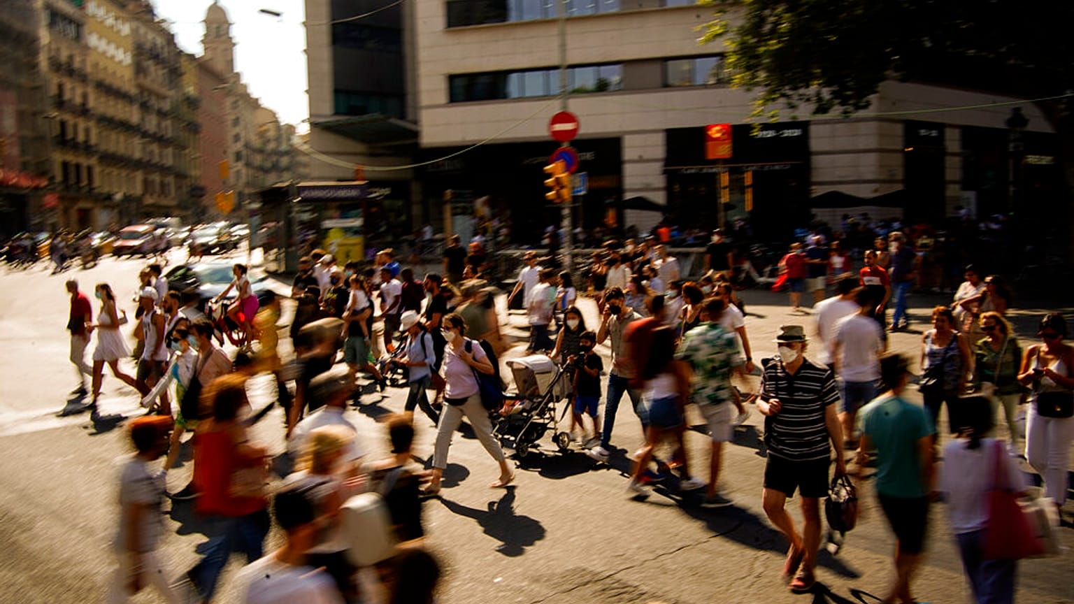 People wearing a face mask to protect against the spread of coronavirus walk along a street in downtown Barcelona, Spain, Saturday, July 3, 2021. 