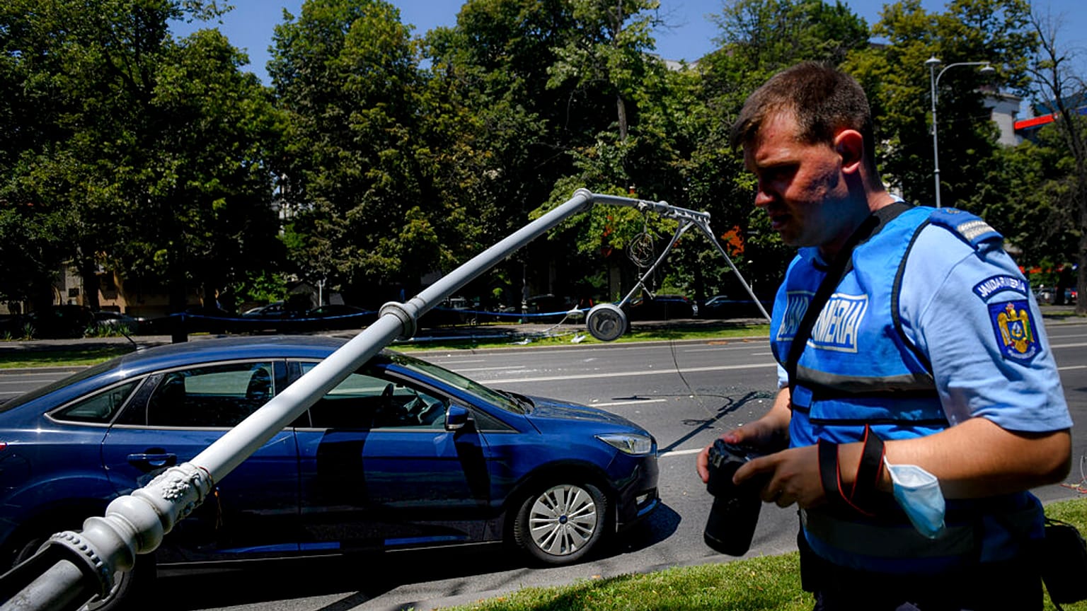 A Romanian gendarme takes pictures of a damaged car after a lamppost was knocked down by a U.S military Black Hawk helicopter following an emergency landing on a busy road