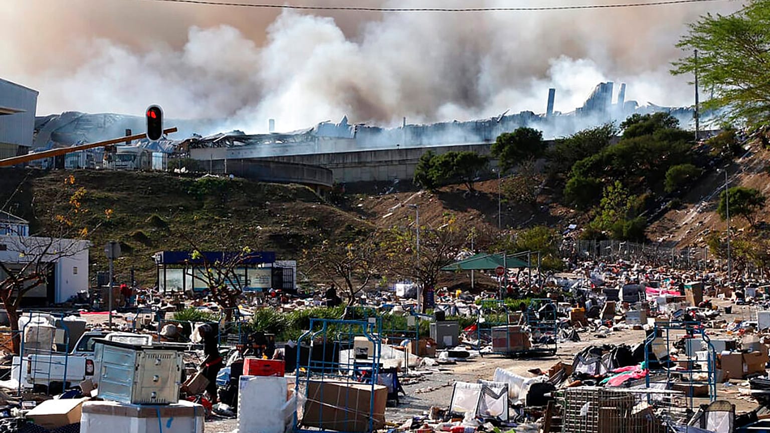 A factory burns in the background while empty boxes litter the foreground from looted goods being removed, on the outskirts of Durban, South Africa
