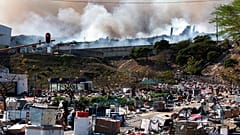 A factory burns in the background while empty boxes litter the foreground from looted goods being removed, on the outskirts of Durban, South Africa