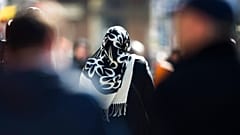 a woman with a headscarf, a traditional dress for Islamic women, walks between other people on a street at the district Neukoelln in Berlin.