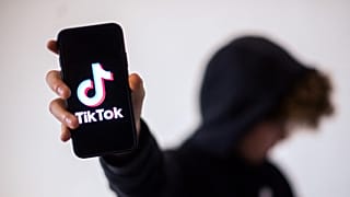 فتىً يحمل في يده جهاز موبايل على شاشته يظهر شعار تطبيق "تيك توك"