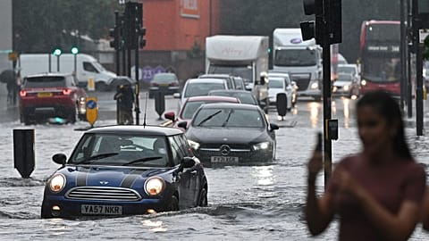 Cars are driven through deep water on a flooded road in The Nine Elms district of London on July 25, 2021 during heavy rain.