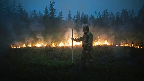 A member of volunteers crew walks past a burning grass near the edge of the fire at Gorny Ulus area west of Yakutsk, Russia, Thursday, July 22, 2021.