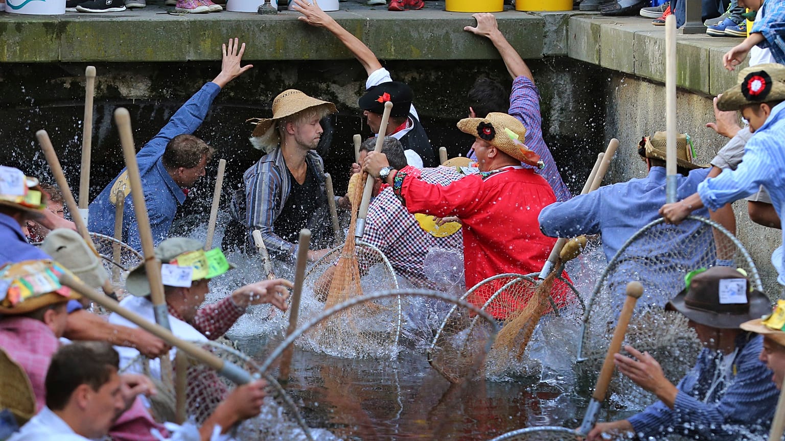Participants of the Fischertag jump with their 'Baeren' hand nets into the ​stream in Memmingen.