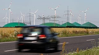 A car passes by a biogas plant and windmills near Nauen, Germany.