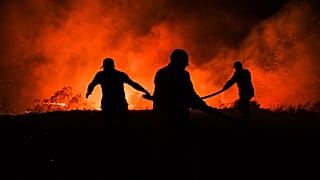 Firefighters and local villagers try to bring a fire under control in the village of Kirli.
