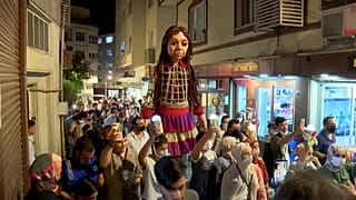 'Little Amal' walking down streets, greeting residents.