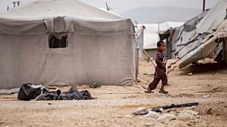 A boy holds a book as he walk at al-Hol camp, which houses families of members of the Islamic State group, in Hasakeh province, Syria, Saturday, May 1, 2021.