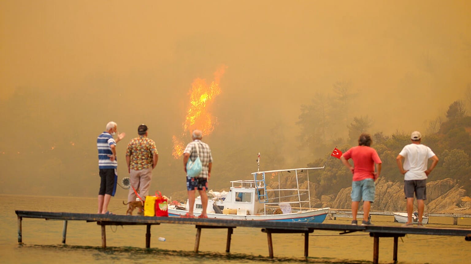 A strandtól méterekre tomboló tüzet nézik egy stégről turisták a törökországi Bodrumnál