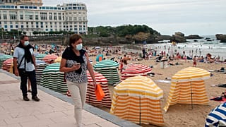People wearing face masks to protect against COVID-19 walk past a beach in Biarritz, southwestern France, July 28, 2021.