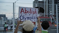 متظاهرون مناهضون للأولمبياد يحملون لافتات أمام السياج حول القرية الرياضية للألعاب الأولمبية الصيفية في طوكيو، اليابان، الجمعة 30 يوليو 2021