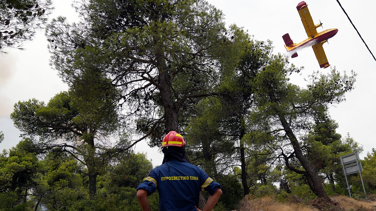 An aircraft operates as a firefighter looks on during a wildfire in Ippokratios Politia village, about 35 kilometres north of Athens, Greece, Aug. 6, 2021. 