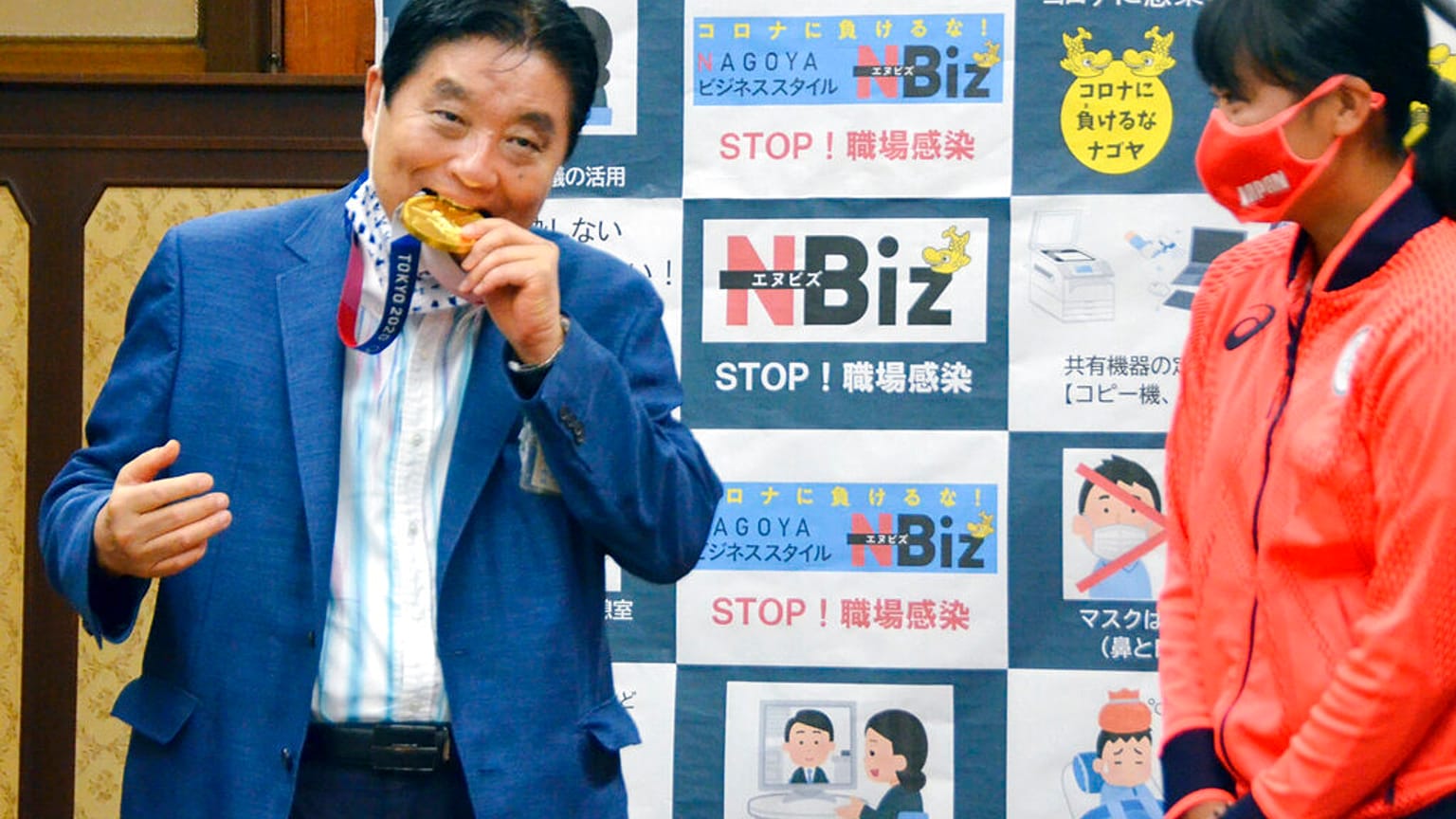 Nagoyas Bürgermeister Takashi Kawamura, links, beißt in die olympische Goldmedaille von Miu Goto, rechts, vom japanischen Softball-Team, 04.08.2021