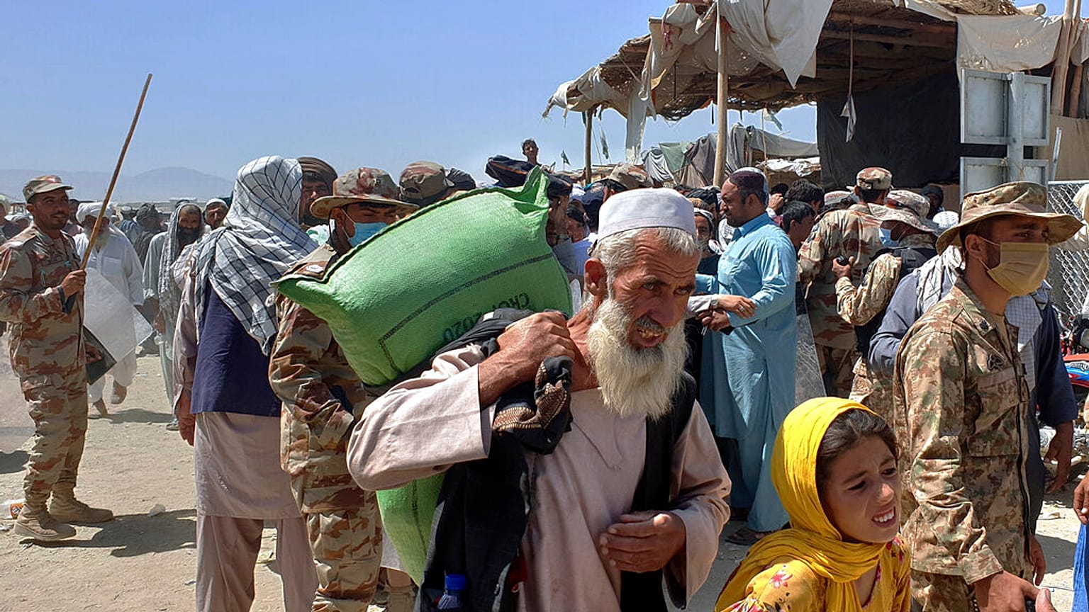 Pakistani soldiers stand guard while stranded people walk towards the Afghan side at a border crossing point, in Chaman, Pakistan, Friday, Aug. 13, 2021