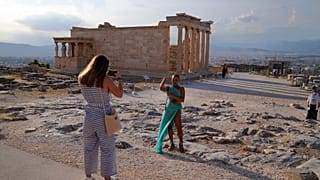 Туристы фотографируются на фоне Парфенона в афинском Акрополе