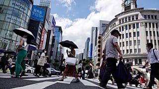 FILE - In this Aug. 10, 2021, file photo, people wearing face masks to help curb the spread of the coronavirus walk under the scorching sun in the Ginza Shopping district.