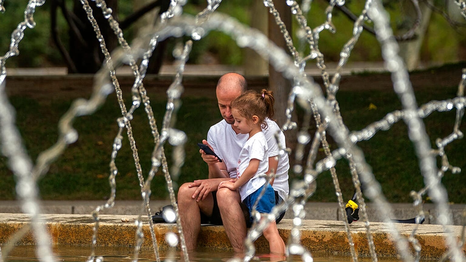 Un padre y su hija se refrescan en una fuente de Madrid, España