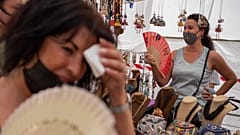 Mujeres se refrescan con abanicos en el mercadillo del Rastro durante una ola de calor en Madrid, España, el 15 de agosto de 2021
