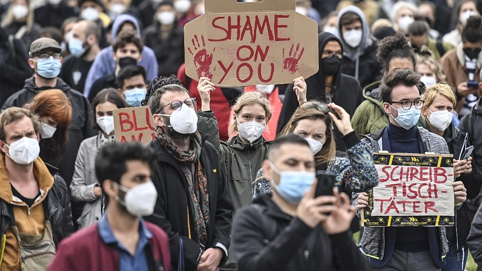 Participants hold up placards reading 'Shame on you' and 'Blood on your hands' as they demonstrate in front of the Reichstag building