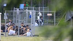Migrants are seen through fences as they sit on the ground in a camp near the border town of Kapciamiestis, Lithuania.