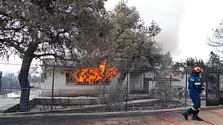 A firefighter extinguish the fire to a house during a wildfire in Thea area some 60 kilometers 