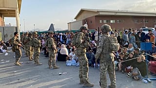 جنود أمريكيون يقفون للحراسة بينما ينتظر الأفغان ركوب طائرة عسكرية أمريكية لمغادرة أفغانستان، في المطار العسكري في كابول في 19 أغسطس 2021 