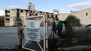 A UN soldier stands by a gate that leads inside the UN buffer zone, Green Line, that divides the Greek, south, and Turkish, north on Jan. 4, 2017. 