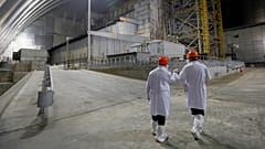 Des employés devant l'ancien réacteur de la centrale nucléaire de Tchernobyl recouvert d'un abri récent, le 15 avril 2021