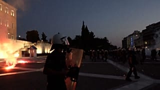 A flare is being thrown toward police officers; smoke in the background.