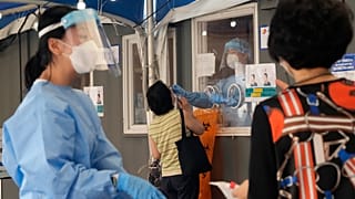 A medical worker in a booth takes a nasal sample from a woman during coronavirus testing at a makeshift testing site in Seoul
