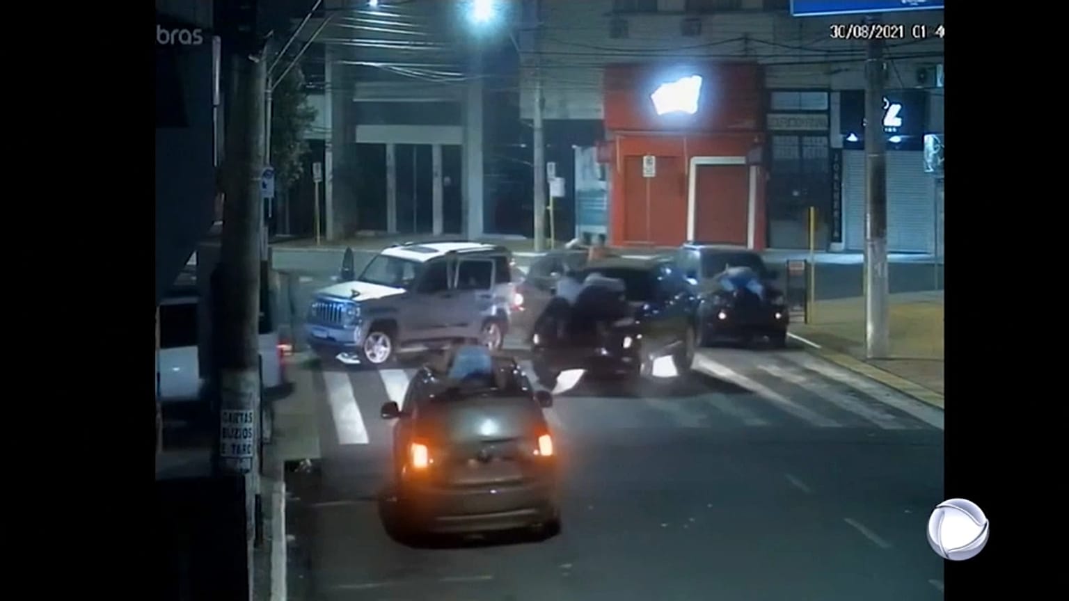 Fermo immagine di una telecamera di videosorveglianza. Si vedono due uomini stesi sul cofano di un'auto in fuga