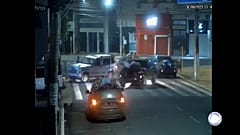 Fermo immagine di una telecamera di videosorveglianza. Si vedono due uomini stesi sul cofano di un'auto in fuga