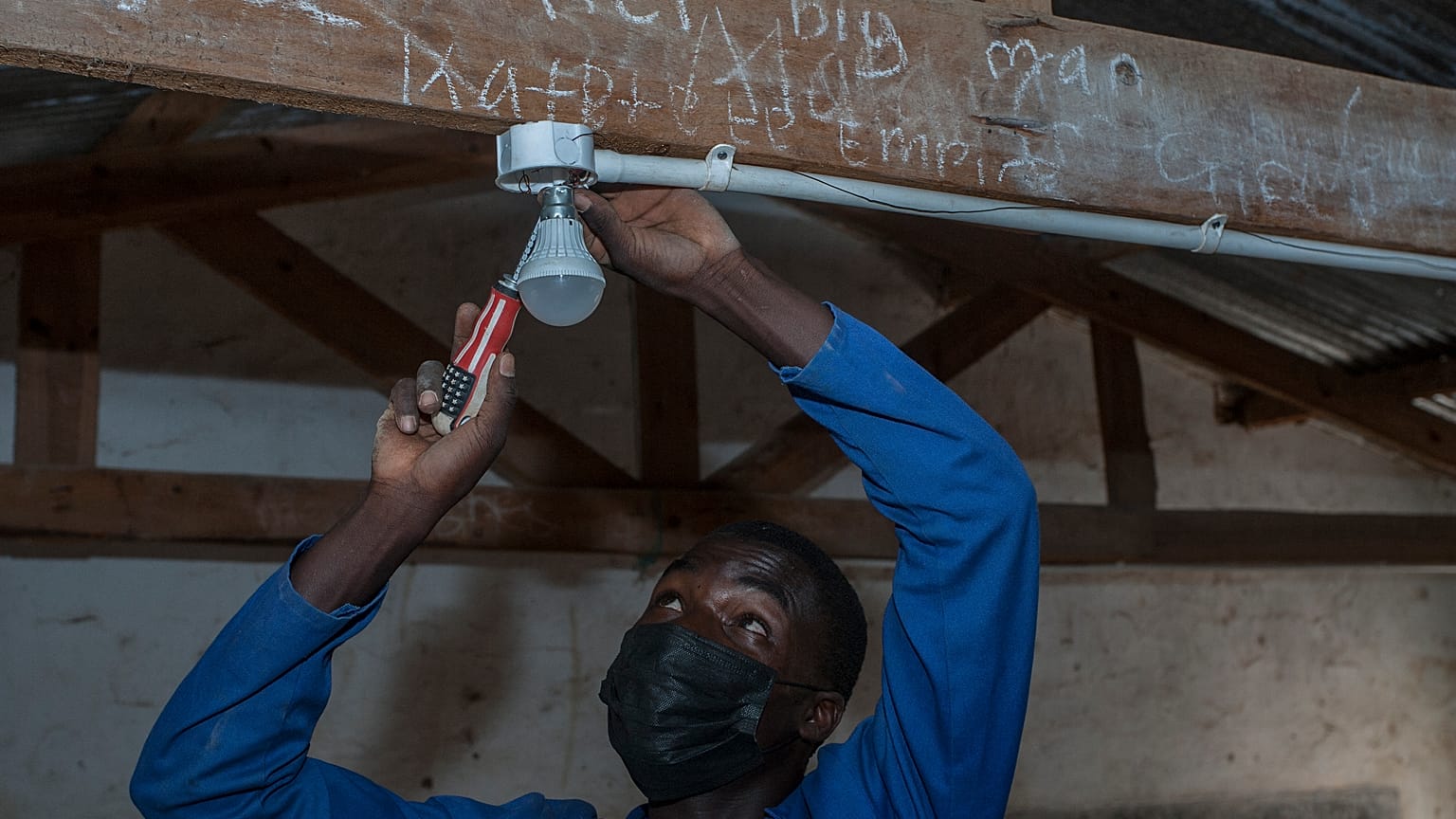 self-taught electricity producer Colrerd Nkosi fixes a bulb in a Standard Eight Class to light the classroom with electricity generated by Nkosi's hydro-powered turbine.