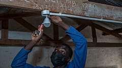 self-taught electricity producer Colrerd Nkosi fixes a bulb in a Standard Eight Class to light the classroom with electricity generated by Nkosi's hydro-powered turbine.