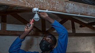 self-taught electricity producer Colrerd Nkosi fixes a bulb in a Standard Eight Class to light the classroom with electricity generated by Nkosi's hydro-powered turbine.