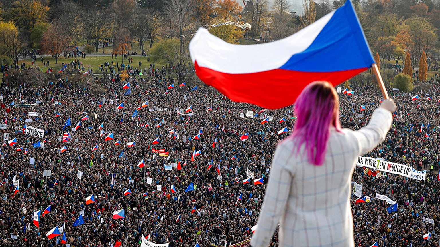A woman waves a Czech flag from a roof as people take part in a large anti-government protest in Prague, Czech Republic, Saturday, Nov. 16, 2019