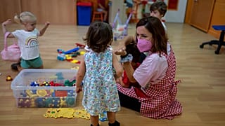 A teacher wearing a face mask to protect against the spread of coronavirus reacts with children in a class, at Vallehermoso school