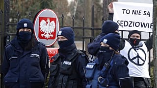 Police surround a protester who holds a sign saying in front of the Constitutional Court in Warsaw, Poland, Wednesday March 10, 2021