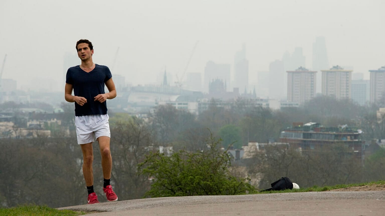 A man jogs up Primrose Hill as buildings in central London stand shrouded in smog.