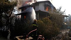 A firefighter tries to extinguish the flames at a burning house 60 kilometers northwest of Athens, Greece