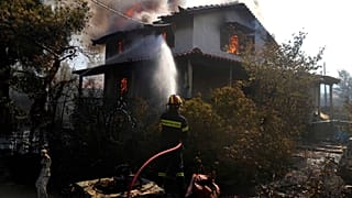 A firefighter tries to extinguish the flames at a burning house 60 kilometers northwest of Athens, Greece