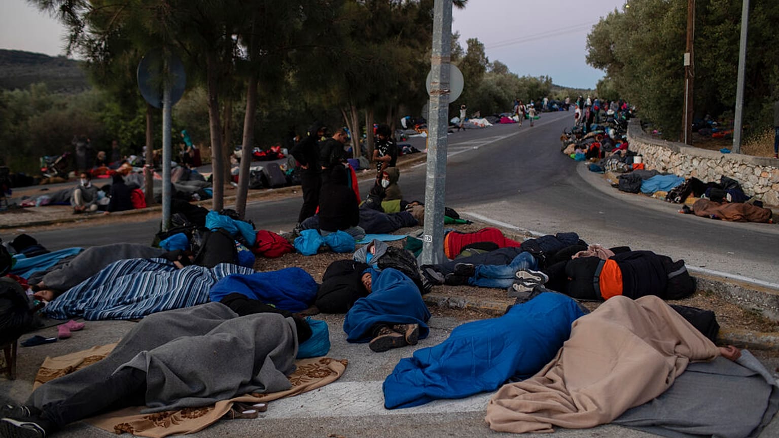 In this Thursday, Sept. 10, 2020, file photo, refugees and migrants sleep on a street near the destroyed Moria camp following a fire, on Lesbos island, Greece.