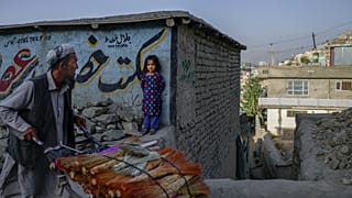 A vendor pushes his handcart loaded with brooms as a girl watches in Kabul.