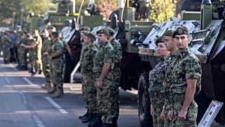 Serbian army soldiers stand to attention in front of armored personnel carriers in Belgrade.