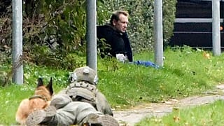 A police office watches Peter Madsen as he sits on the side of a road after being apprehended following a failed escape attempt in Albertslund, Denmark, Oct. 20, 2020.