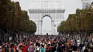 Pedestrians walking along the Champs-Elysees, in front of the Arc de Triomphe wrapped in silver by the late artist Christo.