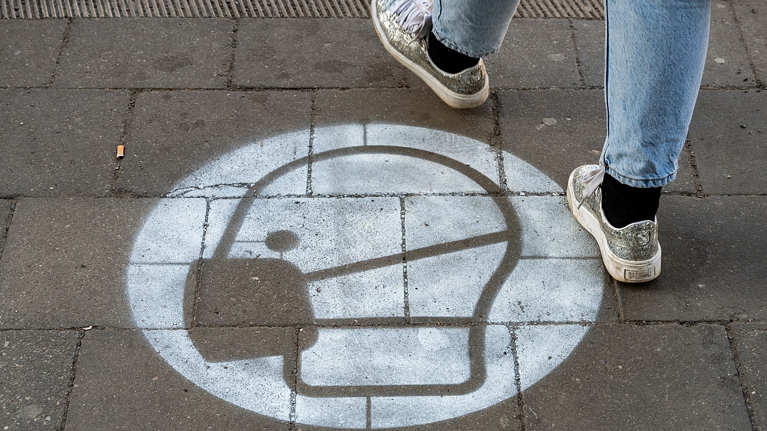 A woman walks past a sign painted on the sidewalk indicating that use of face masks is mandatory, at a busy crossing in Berlin on March 10, 2021